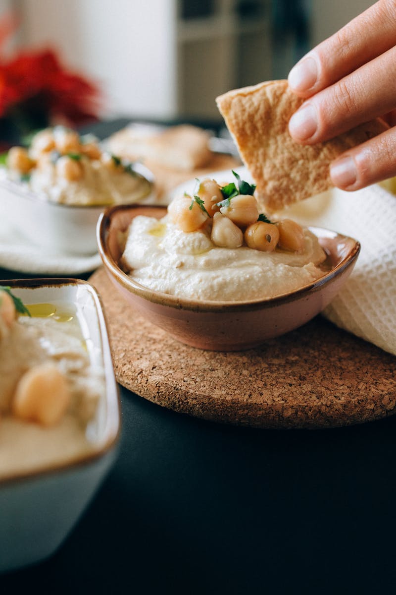 Close-up of a hand dipping pita bread into creamy hummus topped with chickpeas.